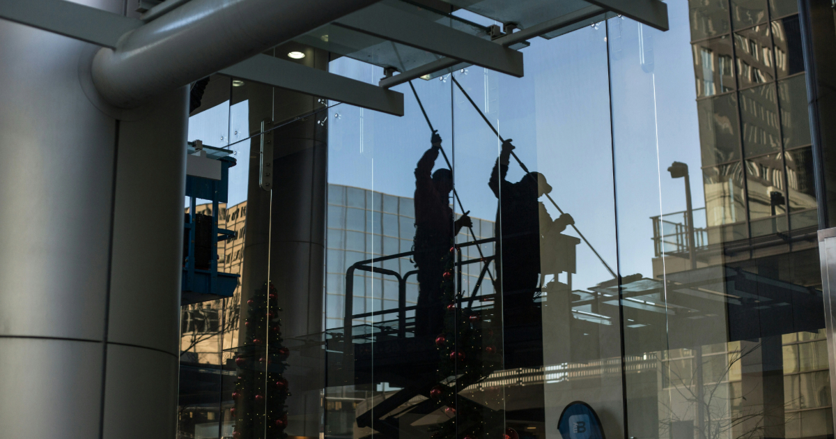 Two installers on an aerial lift working on a floor-to-ceiling commercial glass curtain wall
