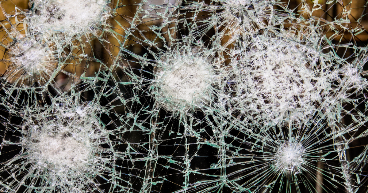 Shattered glass held together in the frame after multiple impacts, with cracks radiating from several separate strike points.